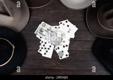 Vieux chapeaux de l'Ouest avec carte à jouer avec des papiers argent et pièces d'argent sur la table. Vue de dessus. Banque D'Images