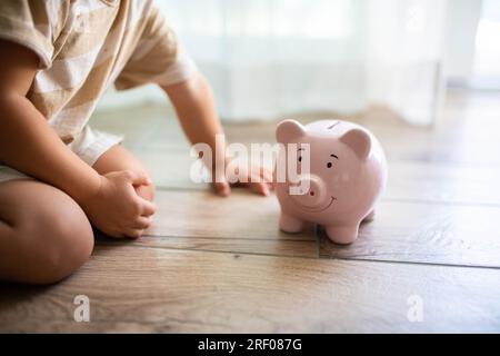 Enfant assis sur le sol près d'une tirelire souriante. Économiser de l'argent pour les enfants concept. Banque D'Images