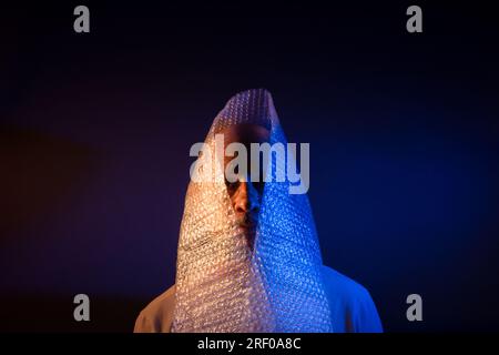 Homme chauve avec une barbe, avec un film de bulles autour de sa tête. Isolé sur fond rouge foncé. Banque D'Images