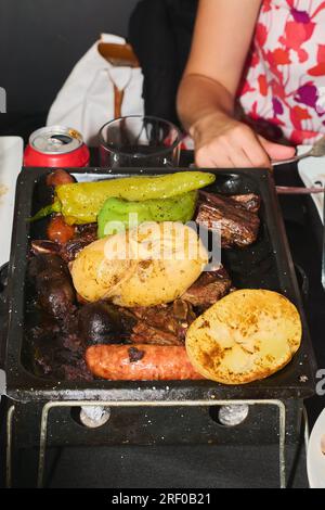 Gros plan de viande avec des légumes assortis sur le gril à charbon et une personne méconnaissable derrière. Alimentation saine et concept de cuisine. Banque D'Images