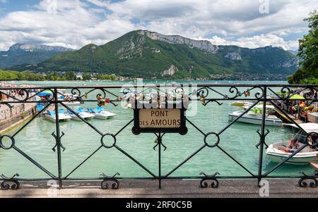 Pont de l'Amour ('Pont des Amours' en français écrit sur le panneau) avec des activités de loisirs et des bateaux naviguant sur le lac d'Annecy en arrière-plan. Banque D'Images