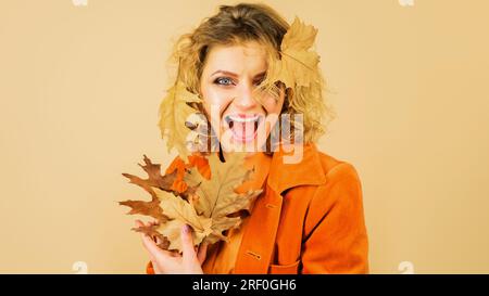 Femme à la mode dans les vêtements d'automne avec des feuilles jaunes. Belle jeune fille avec feuille d'automne. Modèle féminin heureux en manteau orange. Mode automne pour Banque D'Images