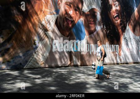 Vienne, Autriche. 28 juillet 2023 : un instantané de la vie urbaine avec des piétons passant devant une bannière vibrante, avec la lumière et l'ombre dansant dans la rue. Banque D'Images