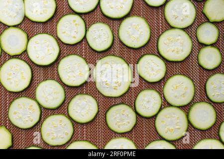 Une photo de pose plate de petites tranches de courgettes disposées sur un tapis séchant au soleil. Banque D'Images