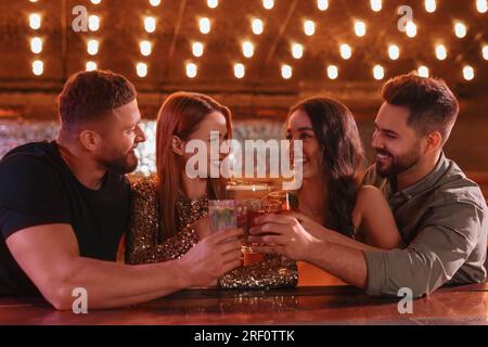 Des amis heureux qui siègent des verres avec des cocktails frais au bar Banque D'Images