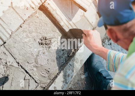 Le carreleur ouvrier pose des carreaux avec du ciment à l'extérieur le jour d'été. Flux de travail authentique. Banque D'Images