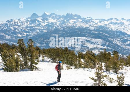 Un randonneur solitaire admire la vaste beauté des sommets enneigés près de Mammoth Lakes sous un ciel bleu clair. Banque D'Images