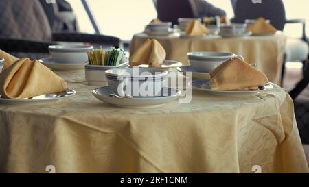 Table servie avec nappe et vêtements de table. Vaisselle à thé et serviette pliée sur des assiettes avec des supplies à sucre disposées au centre de la table. Table servie au repos Banque D'Images