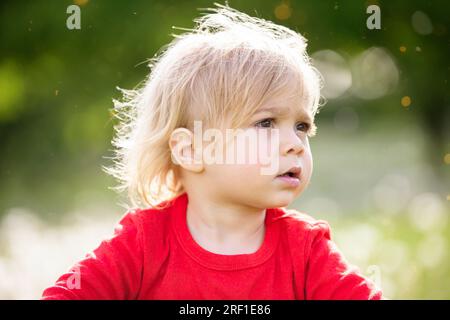 Magnifique enfant blond gros plan sur un fond de verdure estivale. Un petit garçon juif qui ne se fait couper les cheveux qu'à l'âge de trois ans. Banque D'Images