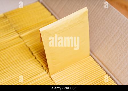 Gros plan d'une boîte en carton ouverte remplie d'enveloppes jaunes rembourrées soigneusement disposées. Une enveloppe est légèrement retirée de la pile. Banque D'Images