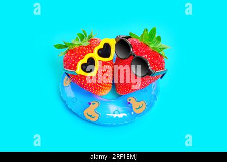 Vue de haut en bas de deux fraises, portant des lunettes de soleil élégantes, flottant sur un flotteur gonflable. Concept dynamique d'escapade estivale rêveuse. Banque D'Images