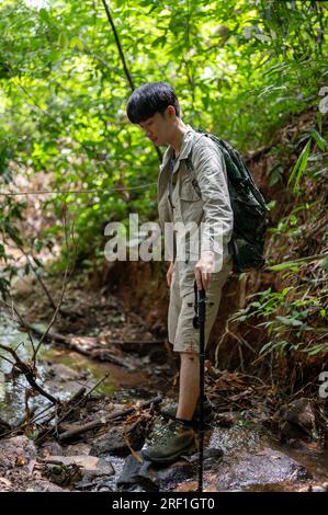 Un portrait d'un randonneur asiatique actif marchant devant un petit ruisseau naturel et profitant de la randonnée dans la forêt verdoyante seule. Banque D'Images