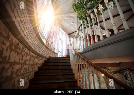 Un escalier en colimaçon avec rampes en bois mène au sommet éclairé par le soleil. Banque D'Images