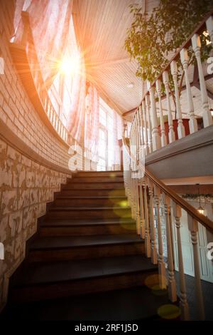 Un escalier en colimaçon avec rampes en bois mène au sommet éclairé par le soleil. Banque D'Images