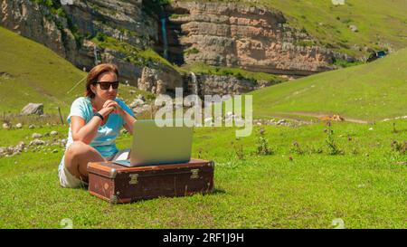 Jeune femme au travail sur un ordinateur portable dans la nature dans les montagnes Banque D'Images