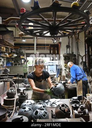 27 juillet 2023, Saxe, Hohenprießnitz : Marika Widdermann, forgeron et dessinatrice de métaux de 39 ans, travaille dans la forge de son père Roger Widdermann sur des boules de feu, qu'elle dessine avec différents motifs. Avec leur forge, l’équipe père-fille est l’une des rares entreprises artisanales pratiquant encore cet artisanat ancien en Allemagne. En plus des objets utilitaires individuels et des bijoux, ils créent également des meubles forgés et des bols et boules de feu pour le recyclage des résidus de cire, qui sont particulièrement demandés pendant les mois d'été, pour les clients au pays et à l'étranger. Photo : Waltraud GRUB Banque D'Images