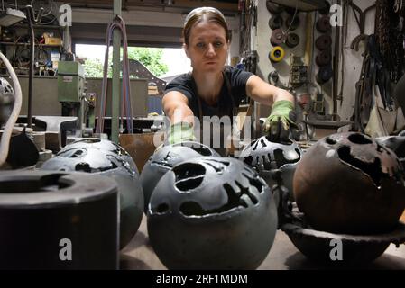 27 juillet 2023, Saxe, Hohenprießnitz : Marika Widdermann, forgeron et dessinatrice de métaux de 39 ans, travaille dans la forge de son père Roger Widdermann sur des boules de feu, qu'elle dessine avec différents motifs. Avec leur forge, l’équipe père-fille est l’une des rares entreprises artisanales pratiquant encore cet artisanat ancien en Allemagne. En plus des objets utilitaires individuels et des bijoux, ils créent également des meubles forgés et des bols et boules de feu pour le recyclage des résidus de cire, qui sont particulièrement demandés pendant les mois d'été, pour les clients au pays et à l'étranger. Photo : Waltraud GRUB Banque D'Images