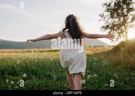 Heureuse petite fille courant sur les montagnes de fond et le ciel au coucher du soleil ou lever du soleil incroyable. Enfant court avec les bras levés comme les ailes d'un avion, childho Banque D'Images