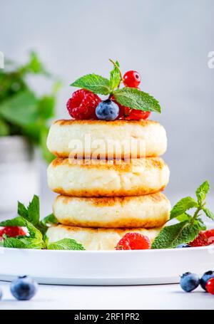 Crêpes épaisses au fromage cottage avec des myrtilles, des framboises et des groseilles rouges, décorées avec de la menthe sur une assiette blanche, délicieux petit déjeuner. Table grise Banque D'Images