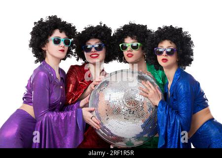 De belles filles en perruques afro et des costumes brillants multicolores tiennent une boule disco. Style disco. Banque D'Images