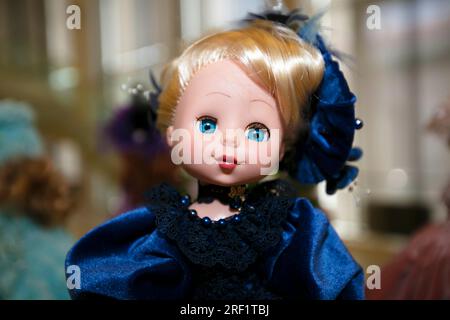 La tête d'un jouet de poupée aux yeux bleus dans de beaux vêtements en gros plan. Banque D'Images