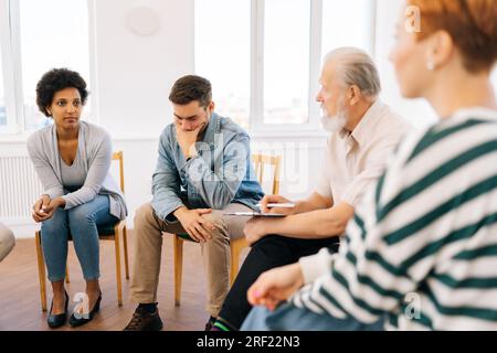 Vue latérale du chef de groupe adulte senior sérieux parlant lors de la réunion de teambuilding. Équipe d'affaires assis sur des chaises en cercle, parlant, discutant Banque D'Images