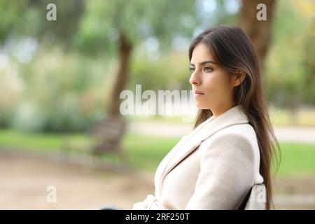 Femme sérieuse en hiver regarde loin sur un banc dans un parc Banque D'Images