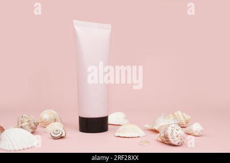 Tube en plastique de bouteille de squeeze rose sans marque avec bouchon noir et beaucoup de coquillages différents sur fond rose. Maquette avec espace de copie. Bouteille cosmétique Banque D'Images