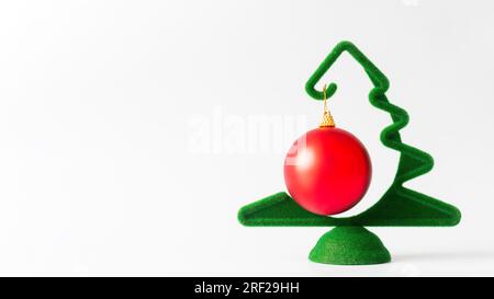 Un petit arbre de Noël vert avec une boule rouge suspendue sur un fond blanc, une bannière, un espace de copie. Carte de nouvel an et de Noël Banque D'Images