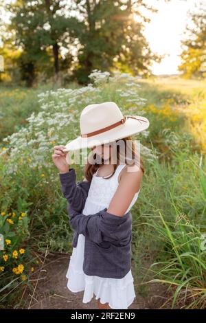 Enfant femelle en robe blanche debout dans les fleurs sauvages au coucher du soleil Banque D'Images