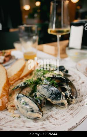 Moules en sauce crème avec pain et vin. Fruits de mer en gros plan. Plat de poisson avec verre de vin. Menu du restaurant de poissons. Moules frites avec coquilles en sauce. Banque D'Images