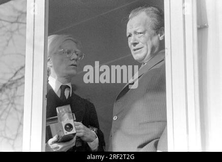 PHOTO D'ARCHIVE : Andy WARHOL aurait eu 95 ans le 6 août 2023, ART/politique Andy WARHOL (à gauche), Etats-Unis et Willy BRANDT, Allemagne, chancelier fédéral (SPD), sont debout devant une fenêtre (de la galerie Wuensche). Brandt regarde par la fenêtre avec une expression sceptique, Warhol se tient dans la pénombre, tient une caméra instantanée dans les deux mains, regarde Brandt inquiet, presque anxieux. Demi-hauteur, photo noir et blanc, format paysage. ? Banque D'Images