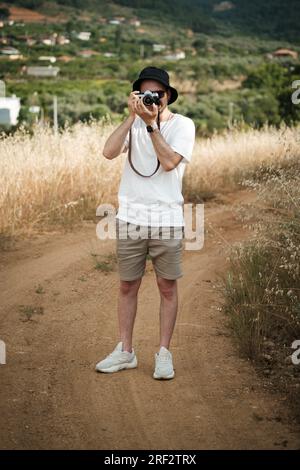 Portrait d'un homme d'une vingtaine d'années, habillé de façon décontractée d'un t-shirt blanc, d'un short beige, de lunettes de soleil et d'une casquette de marin noire, avec un camouflage classique Banque D'Images