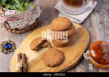 Biscuits aux raisins secs d'avoine sur une planche de bois avec des bâtons de cannelle (Cassia) et une tasse de lait. Pâtisserie traditionnelle maison dans un style rustique. Mise au point sélective Banque D'Images