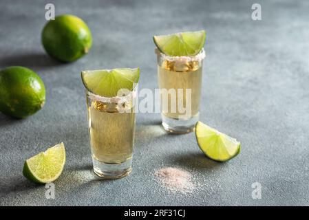 Deux clichés de tequila avec citron vert et sel rose, fond de pierre grise. Vue latérale, mise au point sélective, espace de copie. Banque D'Images