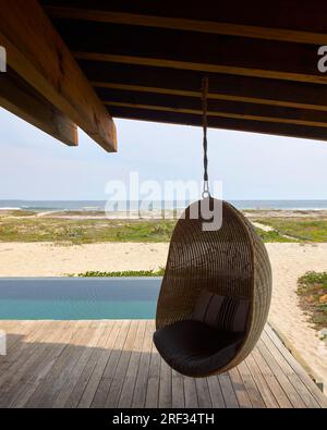 Chaise suspendue en osier avec vue de la piscine à l'océan. Punta Pajaros, Oaxaca, Mexique. Architecte : Alberto Kalach, 2019. Banque D'Images