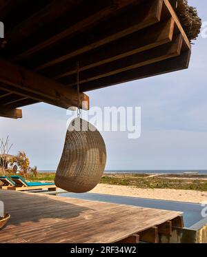 Chaise suspendue en osier avec vue de la piscine à l'océan. Punta Pajaros, Oaxaca, Mexique. Architecte : Alberto Kalach, 2019. Banque D'Images