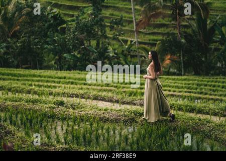 Belle fille en robe verte marchant sur la terrasse de riz. Dame élégante visitant la plantation de riz Banque D'Images