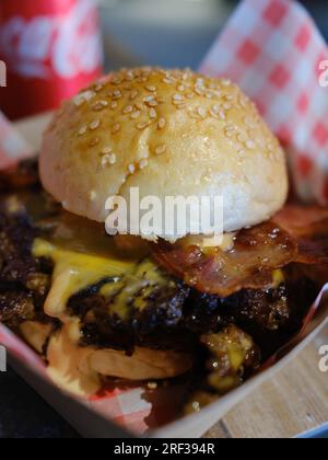 Cheeseburger double bacon servi sur une serviette à carreaux rouge et blanc dans un panier à emporter. Banque D'Images