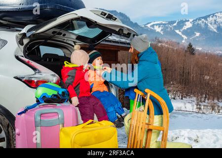 Mère aider à habiller les enfants assis dans le coffre de voiture au-dessus de la montagne de neige Banque D'Images