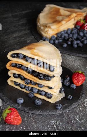 photo crêpes minces frites avec des fraises juteuses mûres et des myrtilles sur fond gris Banque D'Images