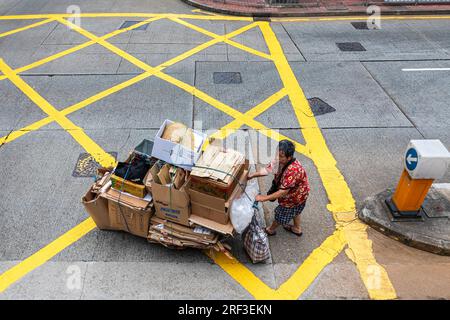 Vieille dame chinoise poussant le chariot à travers la jonction routière tout en recyclant les déchets à Hong Kong, SAR, Chine Banque D'Images