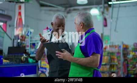 Deux heureux divers cadres supérieurs du magasin frocery vérifiant les opérations d'inventaire avec le dispositif de tablette, les employés plus âgés du supermarché riant et souriant Banque D'Images