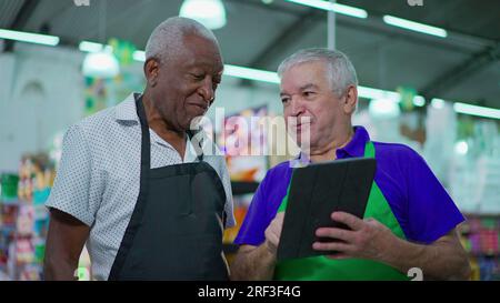 Deux heureux divers cadres supérieurs du magasin frocery vérifiant les opérations d'inventaire avec le dispositif de tablette, les employés plus âgés du supermarché riant et souriant Banque D'Images