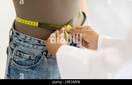 Femme caucasienne mature médecin nutritionniste en manteau blanc mesure la taille du patient avec un ruban à mesurer Banque D'Images