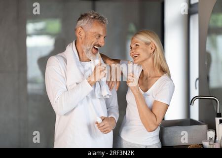 Heureux conjoints matures ayant du plaisir tout en se brossant les dents dans la salle de bain ensemble Banque D'Images
