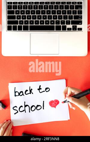 Retour à l'école la main de l'enfant écrit dans un papier sur fond rouge. Banque D'Images