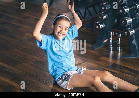 Petite fille utilisant des sangles de fitness trx pour travailler avec son propre poids. Banque D'Images