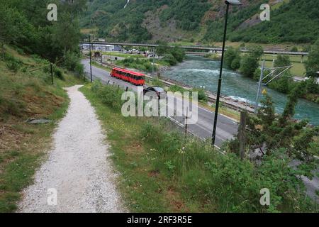 Un train terrestre touristique et une voiture à côté du chemin de fer et de la rivière Flamselvi dans la vallée de Flamsdalen à Flam dans l'ouest de la Norvège. Banque D'Images