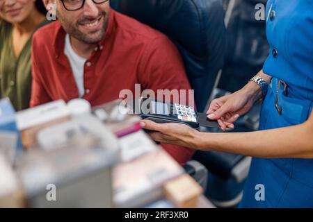 Gros plan sur l'hôtesse de la compagnie aérienne qui tient le terminal alors que le passager homme est enjoué et effectue le paiement Banque D'Images